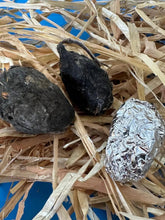 Owl Pellets  of various sizes laid on straw with one wrapped in foil to be shipped.