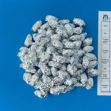A collection of small owl pellets displayed on aluminum foil with a bone matching chart placed next to them on a blue surface.
